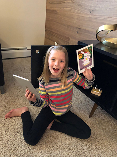 A girl holding up an owl picture and smiling.